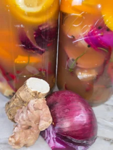 Jar of homemade fire cider with ginger, garlic, lemon, and hot peppers.